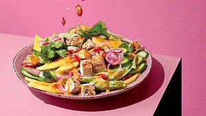 A pink bowl of Chicken Salad with Peanut Butter and Curry Dressing on a pink table against a pink background