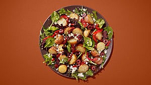 Salad with potatoes, olives and feta on a brown bowl on a brown table.