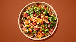 Leafy salad with halloumi cheese, pommegranate and figs in a brown bowl on a brown table.