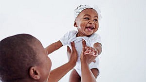 A parent holds their laughing baby up in the air.