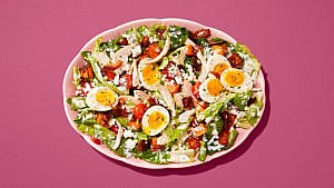 Cobb salad with sliced soft-boiled eggs, tomatoes and chicken in a pink bowl on a pink table.