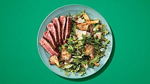 A salad with sliced beef, greens and mushrooms on a green plate on a green table.