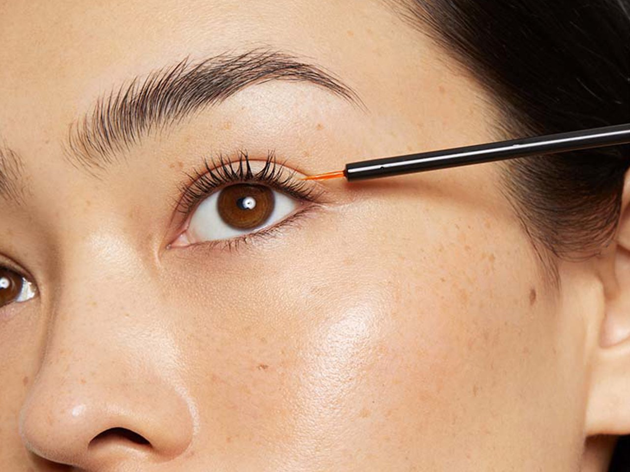 A model seen close-up applying lash serum to her lash line with a small brush.