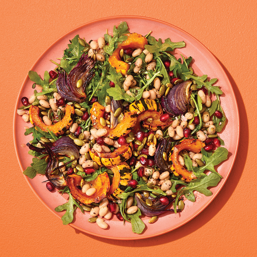 Colourful salad with beans, arugula and squash on an orange plant on an orange table.