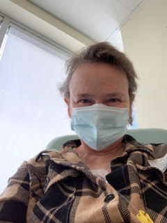 A woman taking a selfie, wearing a blue medical mask and a flannel shirt.