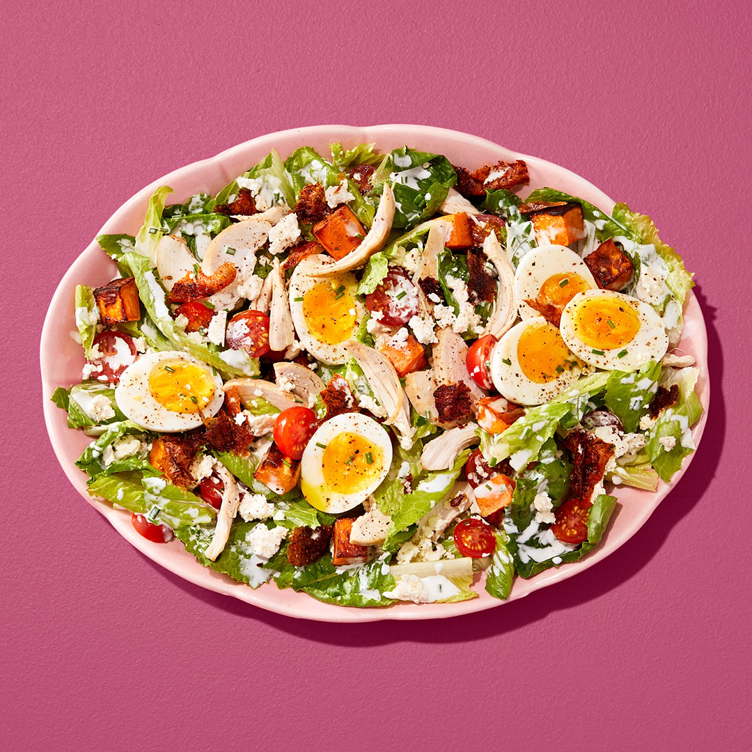 Cobb salad with sliced soft-boiled eggs, tomatoes and chicken in a pink bowl on a pink table.