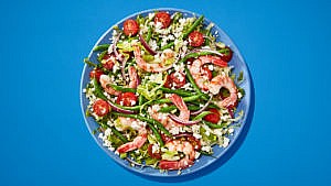 Green bean salad with shrimp and tomatoes on blue plate on blue table.