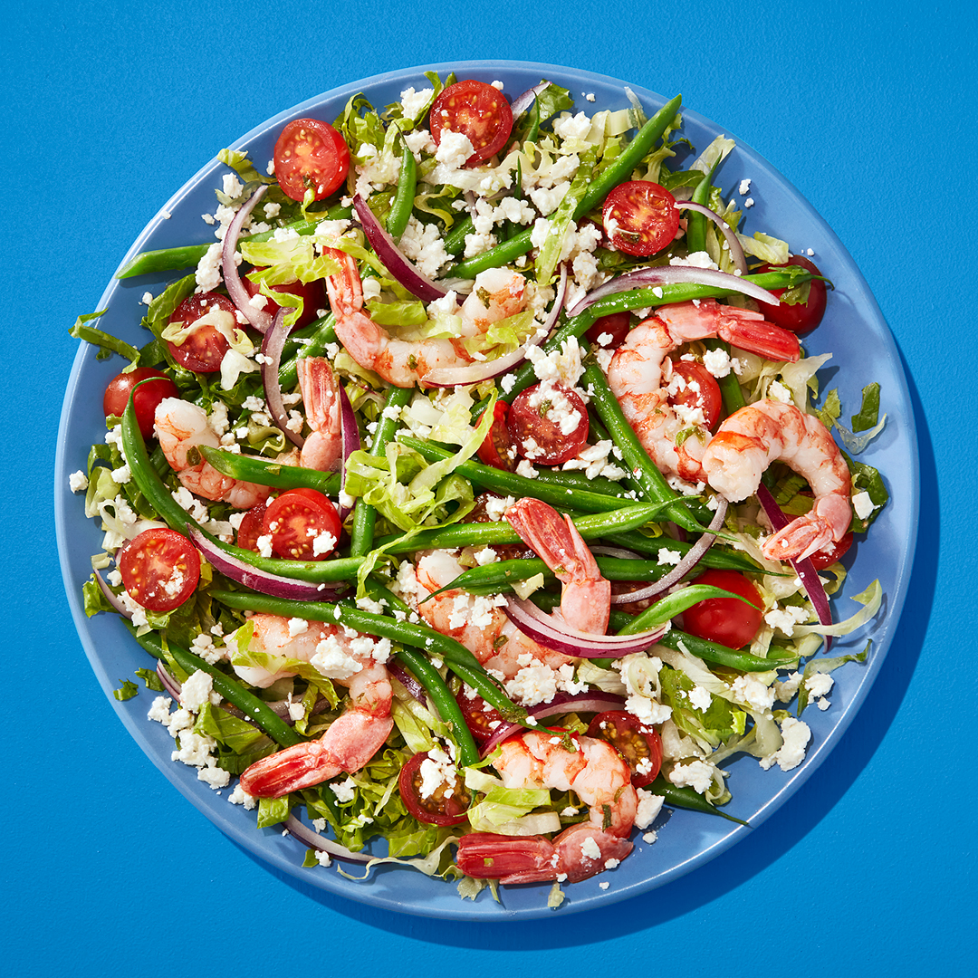 Green bean salad with shrimp and tomatoes on blue plate on blue table.
