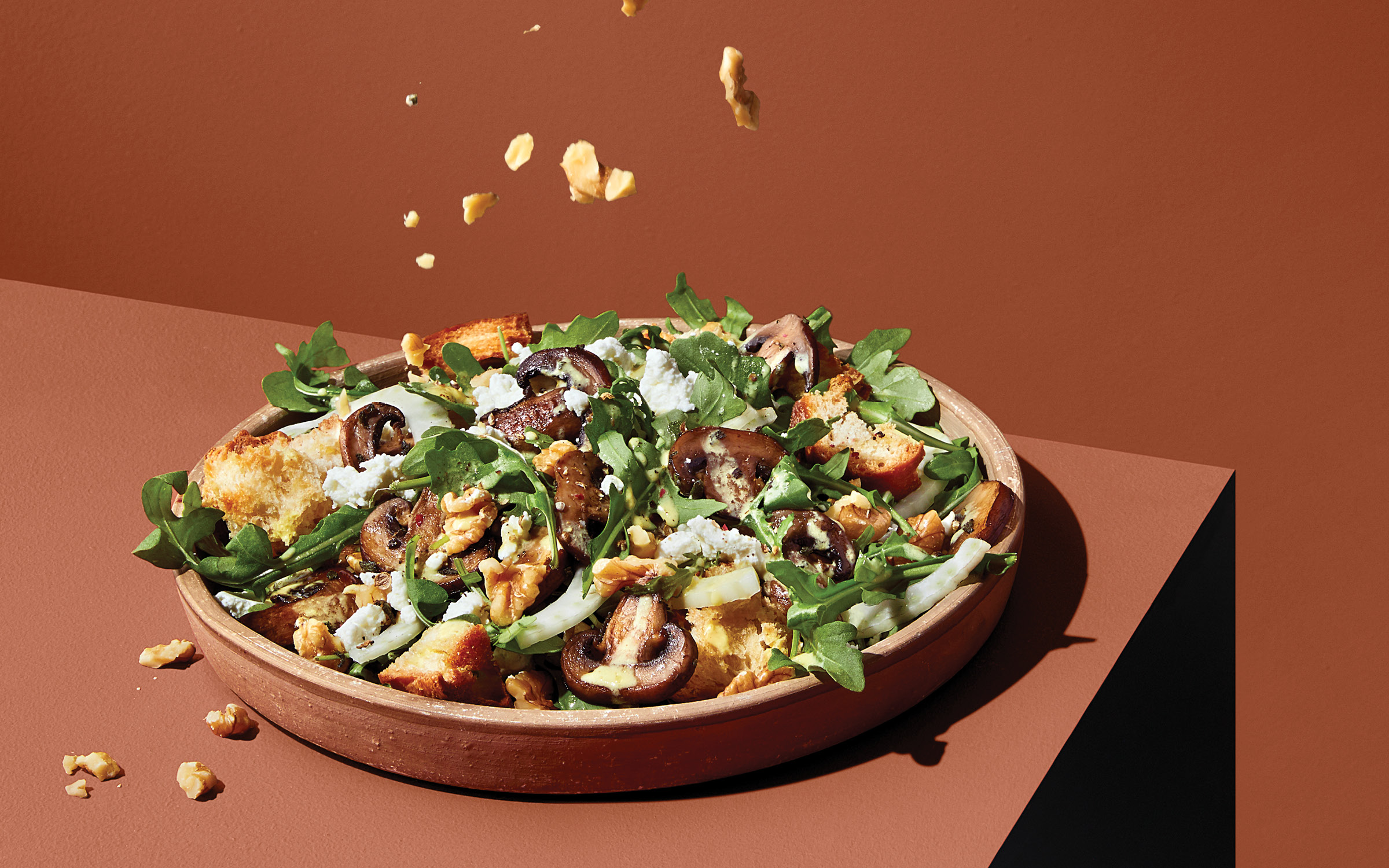 Salad with mushrooms, cheese and nuts in a brown bowl on a brown table.