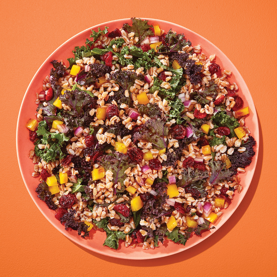 Salad with kale, cranberries, chopped onion and wheatberry on an orange plate on an orange table.