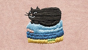 A photo of an embroidery of a black cat sitting on top of a laundry pile against a pink fabric background.