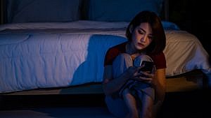 Nighttime scene of woman sitting on the floor looking at her phone