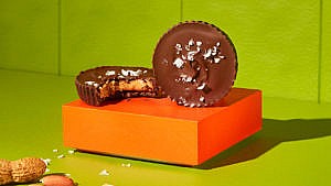 No-bake plant-based salted peanut butter cups, two one with a bite taken out of it on an orange box on a green background