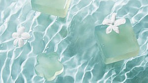 Three Dew Mighty solid skincare serum bars pictured against a watery blue background and decorated with white floral petals.