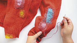 Bright pink, blue and yellow mended patches on a red sweater