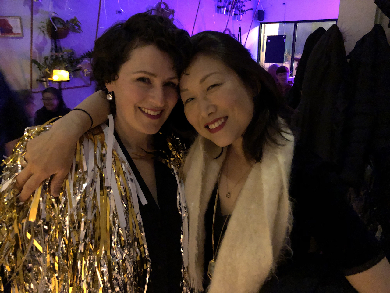 A photo of two smiling women in party clothes against a purple light