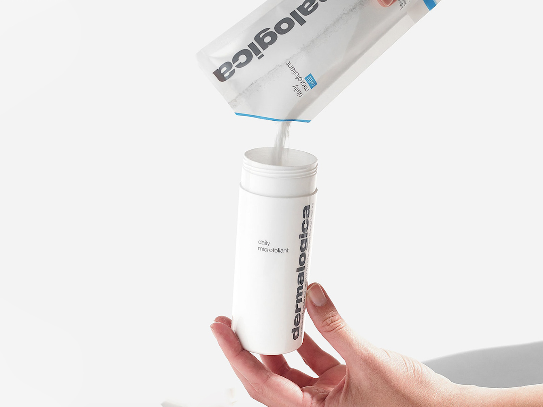 A hand holding a bottle of Dermalogica's Daily Microfoliant as it is being refilled, for an article on the best refillable beauty products
