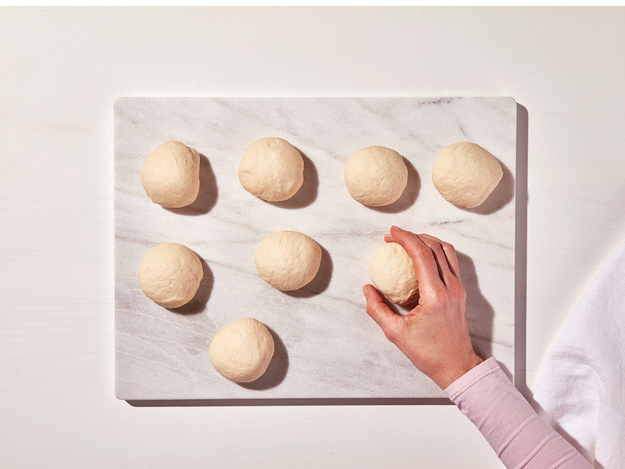 A person's hand placing dough balls on a cutting board, the first step of making homemade bagels.
