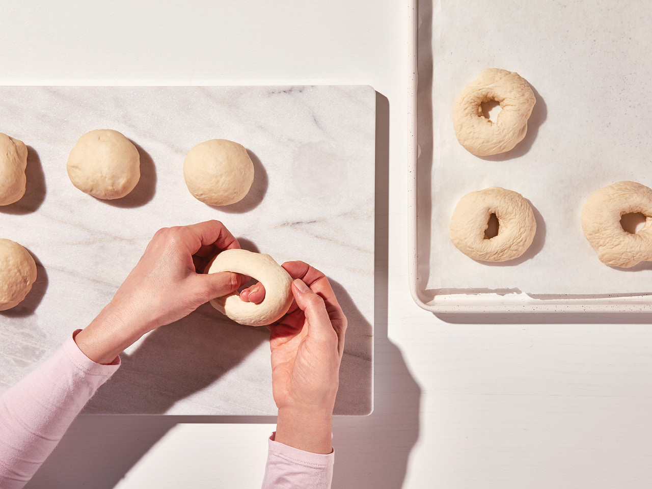 A photo of a person's hands poking a hole into a ball of dough to make homemade bagels.