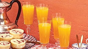 Five glasses of hard cider mimosa served on a table alongside a pitcher and bruch pastries