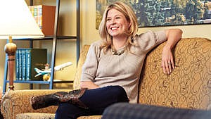A portrait of politician, Michelle Rempel Garner, smiling while sitting on a couch in a warmly-lit room