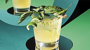 A Rescue Op cocktail served in a glass with a sprig of basil, lime peel, and chili.
