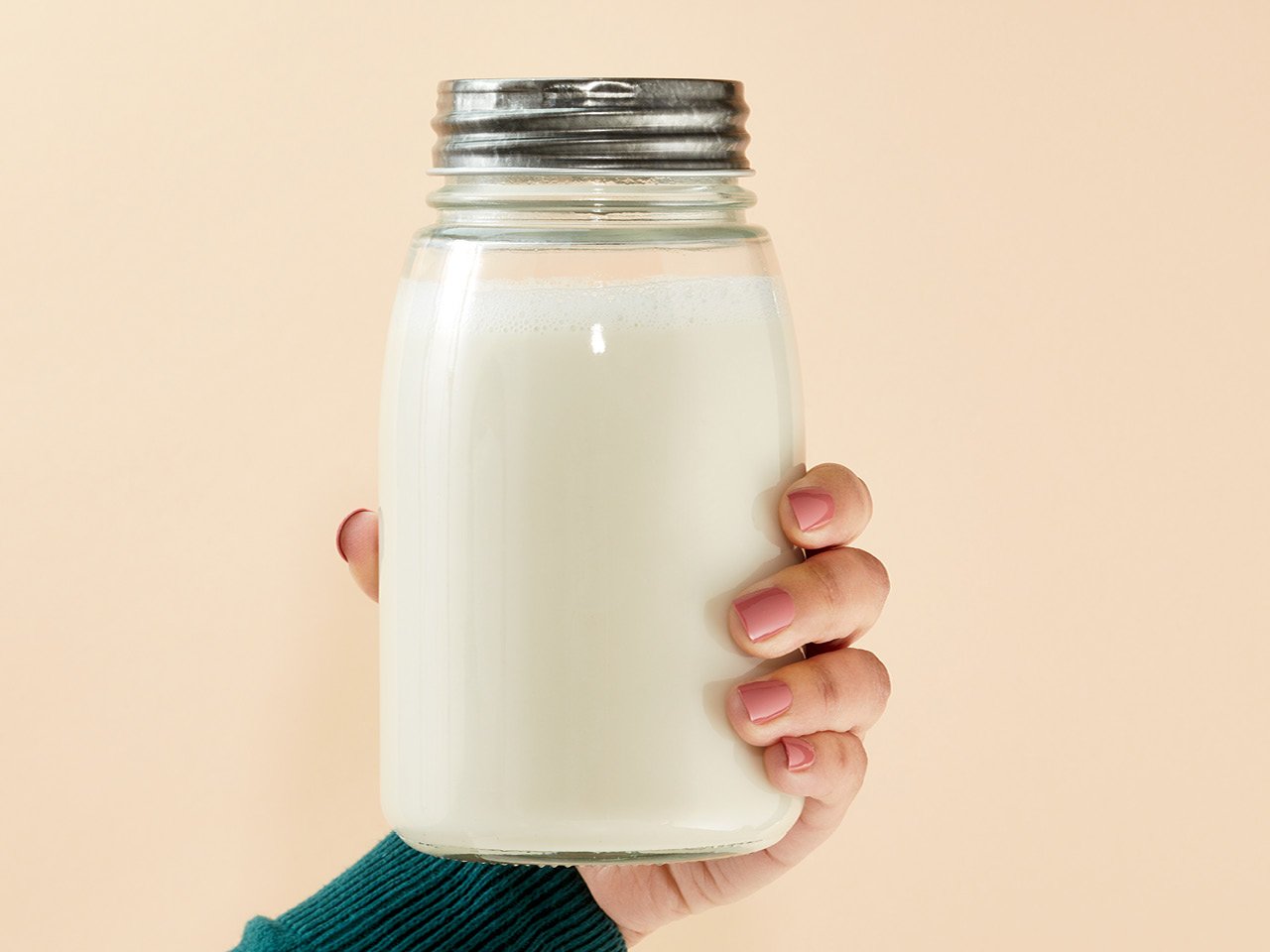 Nut milk recipes: A person's hand holding a mason jar filled with nut milk 