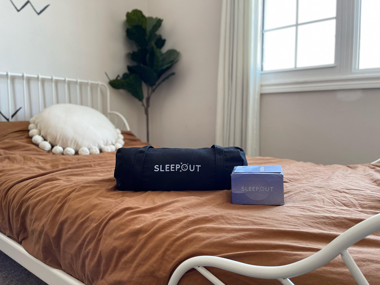Sleepout navy bag and box on top of a bed with brown bedsheets. 