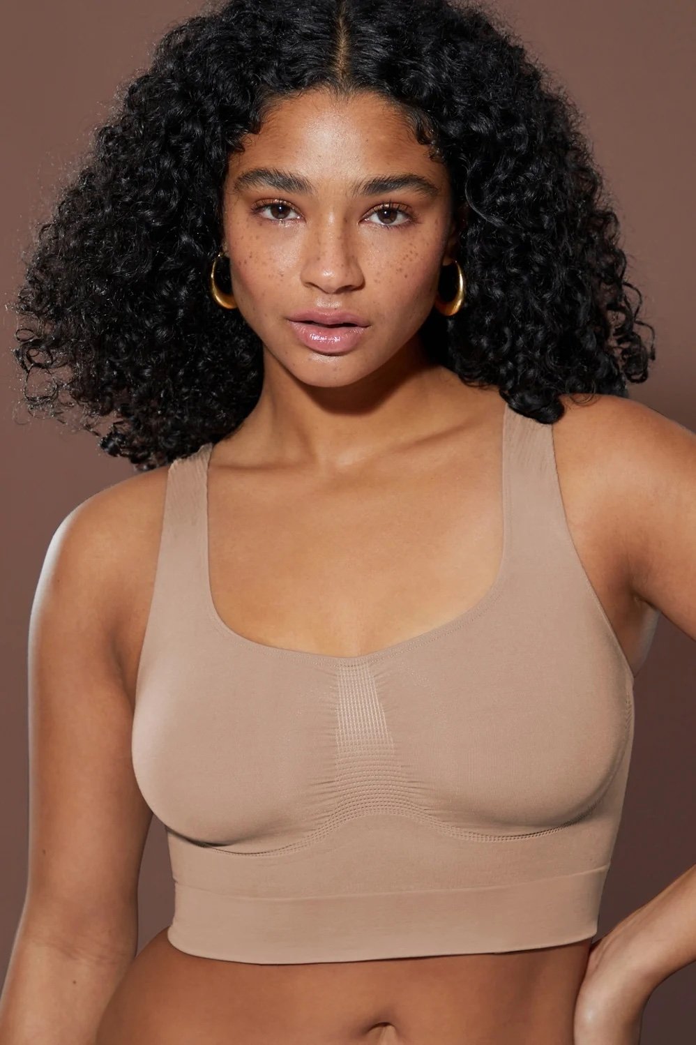 A woman wearing the Nearly Naked Shaping Midi Bra from Yitty, Lizzo's shapewear line