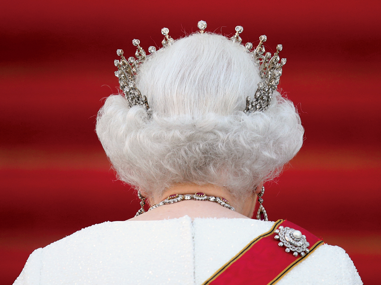 A photo of the back of Queen Elizabeth's head, against a red background