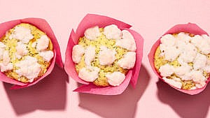 Five lemon poppy seed streusel muffins in pink wrappers on pink backdrop.