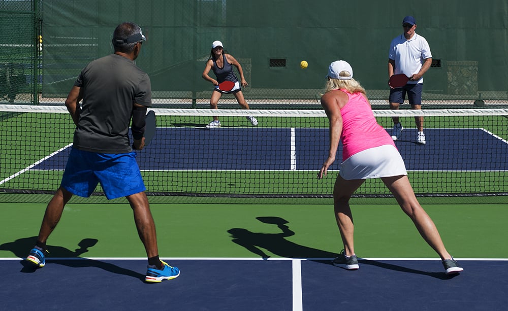colorful action image of two couples playing Pickleball
