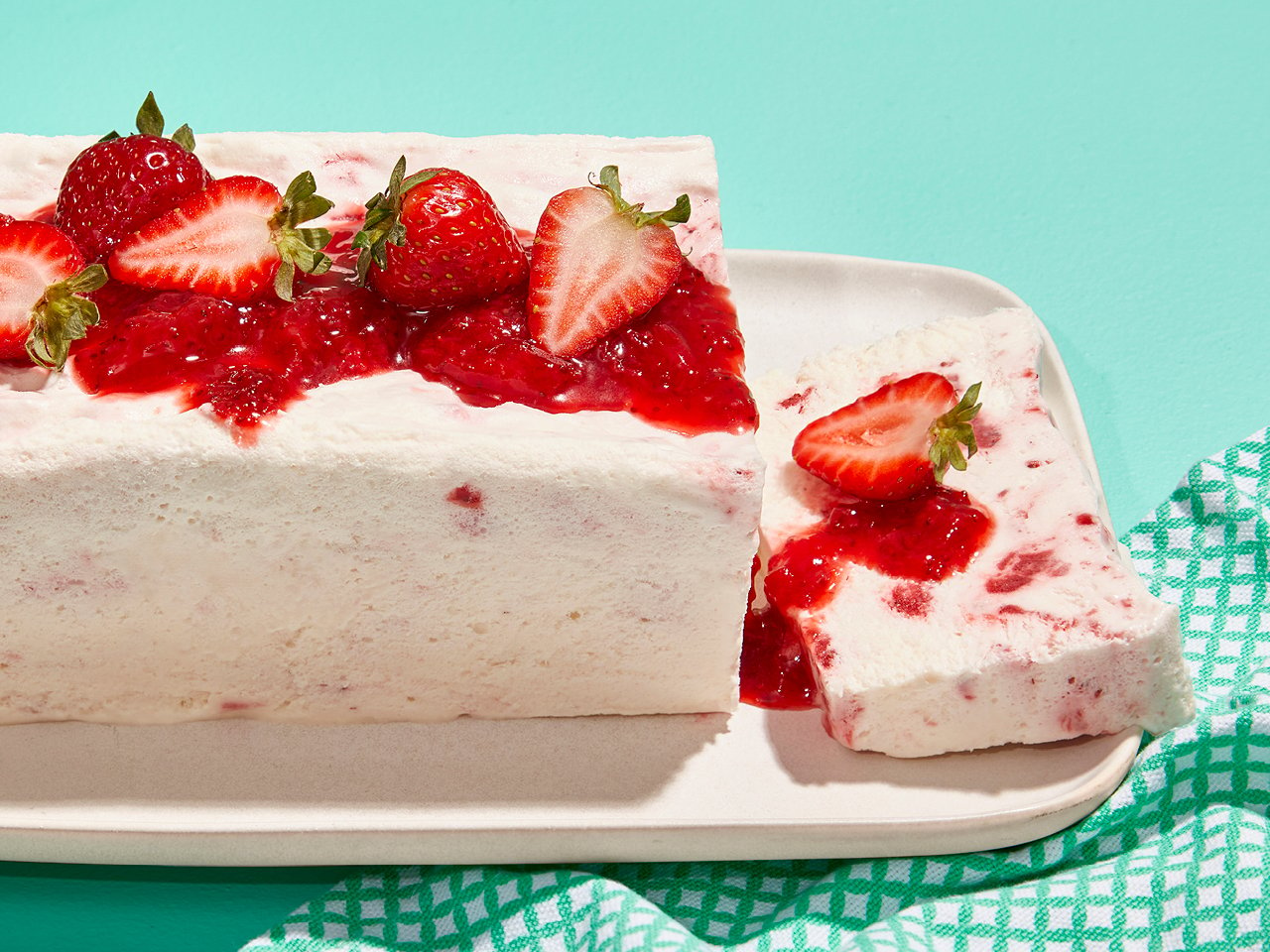 Strawberry and honey semifreddo with a slice sliced off and lying on a cutting board, topped with strawberry compote