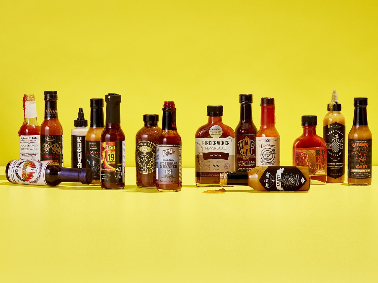 15 bottles of various hot sauces against a bright yellow backdrop