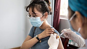 A woman pulls her shirt sleeve up while she's getting a COVID-19 vaccine shot from a healthcare worker