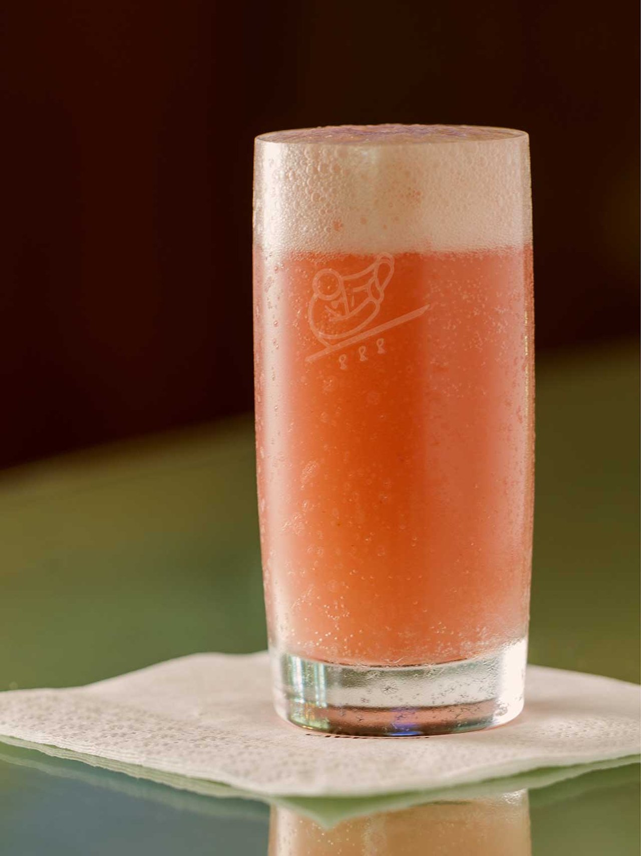 A peach coloured drink in a tall glass resting on a white napkin 