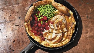 A pan with a savoury Dutch baby filled with chicken, peas and cranberries wooden work surface.