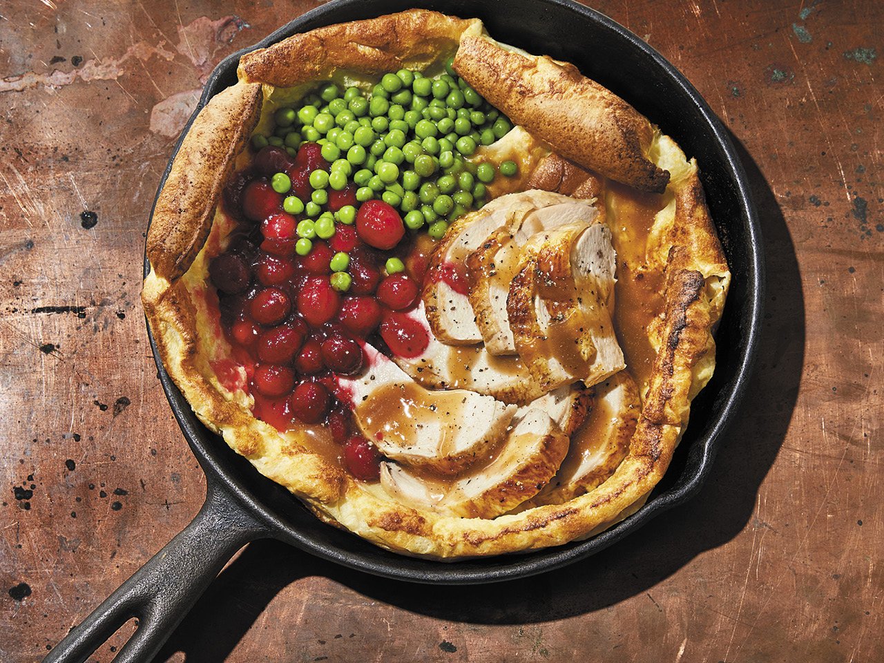 A pan with a Dutch baby filled with chicken, peas and cranberries wooden work surface.
