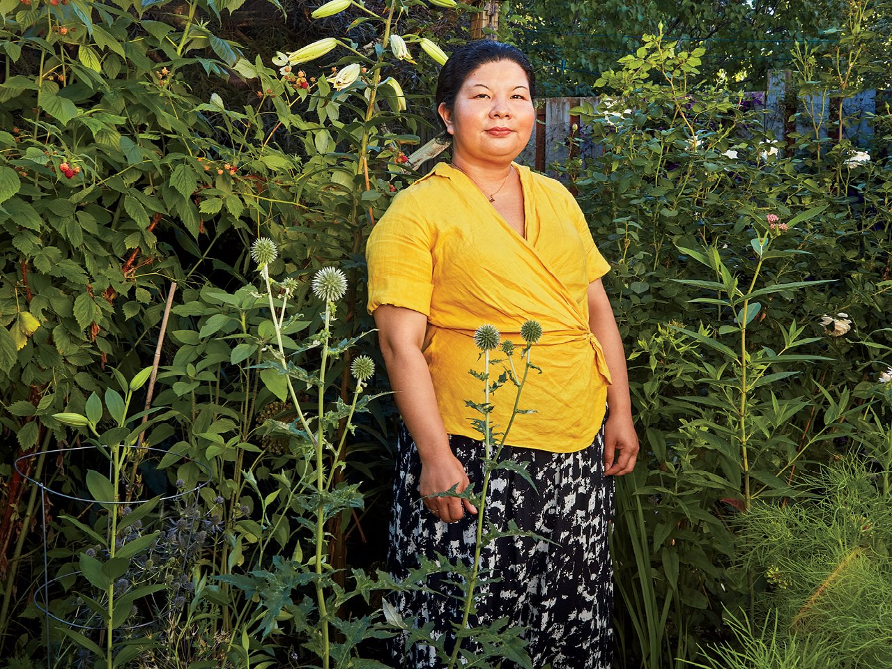A photo of a woman in a yellow shirt, standing among tall vegetation.
