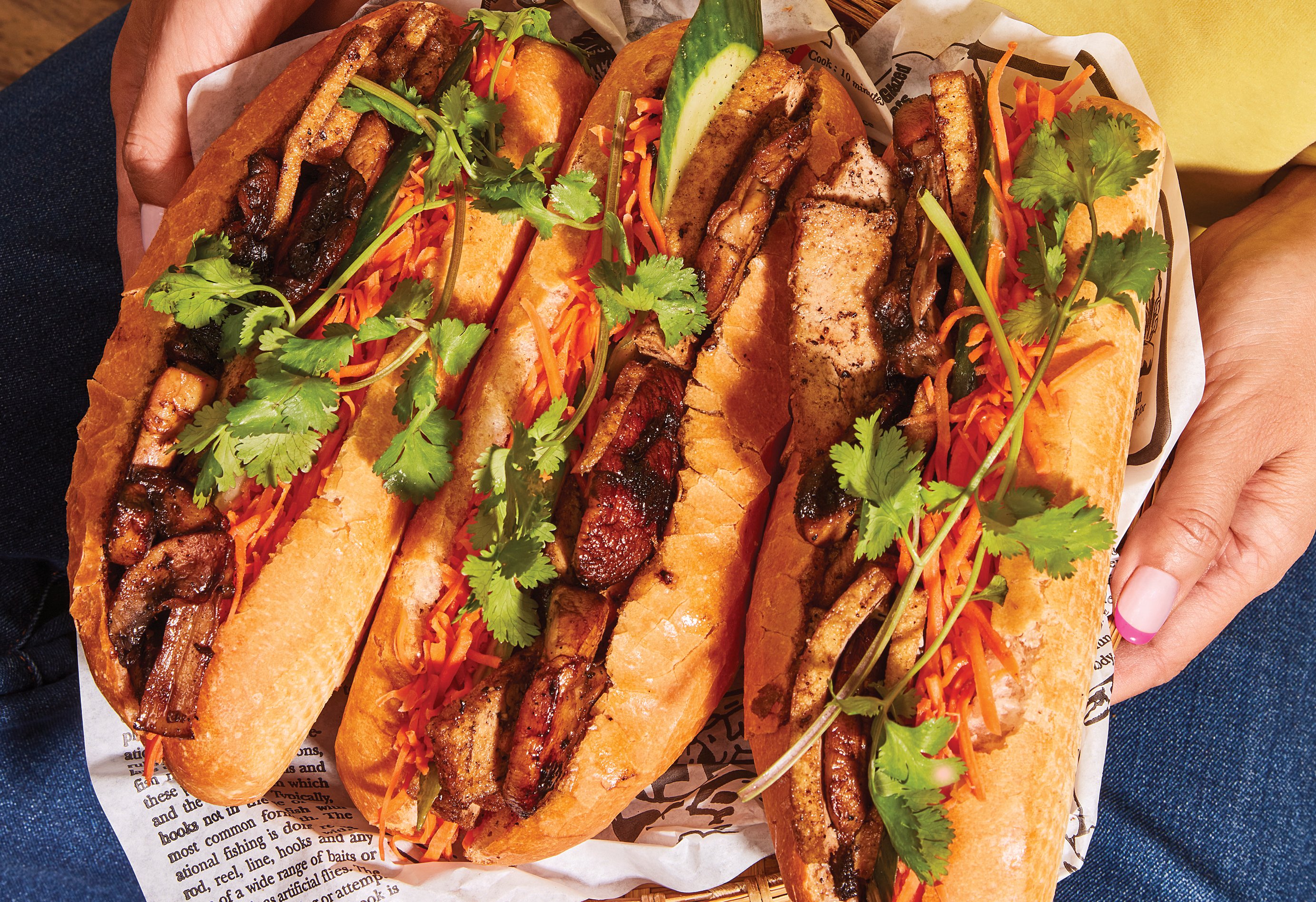 Woman holding three banh mi sandwiches that are partially open in a tray