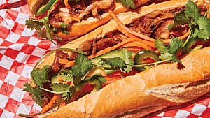 Two banh mi in semi open buns with browned mushrooms and cilantro twigs, placed against a red checkered paper.