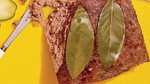 Brown liver pate with two bay leaves on top and a butter knife