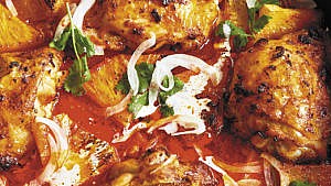 close up of cooked chicken pieces mixed in a brown red sauce with streaks of white sauce and green leaves on top.