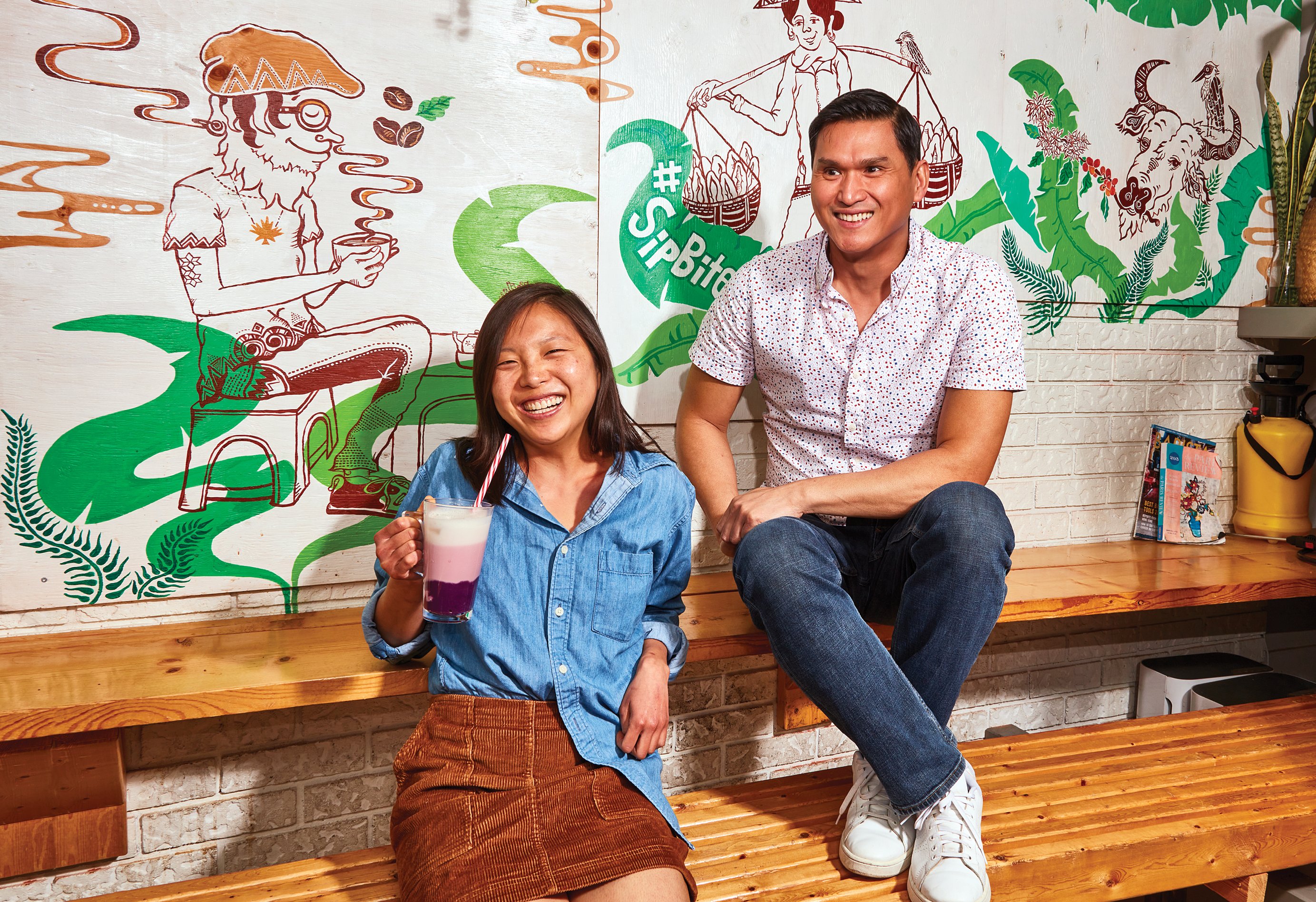 Two restaurant owners sit on a bench in front of a wall with colourful wallpaper