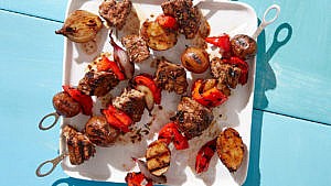 Steak Skewers with potatoes and red peppers and shallots on a white plate on a pale blue table
