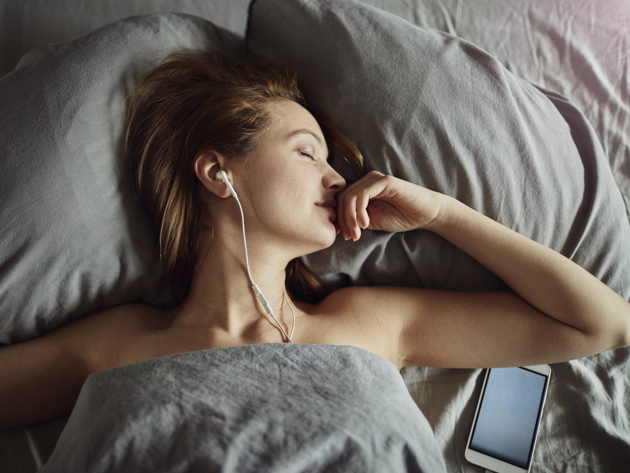 Photo of a woman sleeping with headphones on and her phone next to her