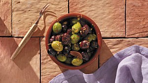 Marinated olives with citrus and fennel seeds served in a dish beside a deli fork