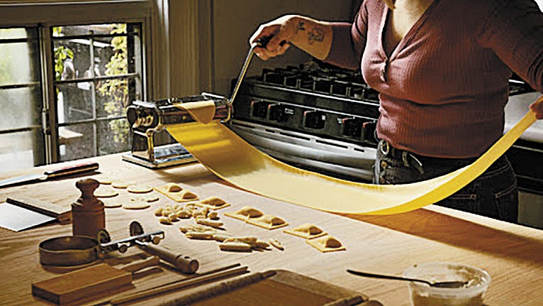 a woman at a wooden table rolling pasta sheets