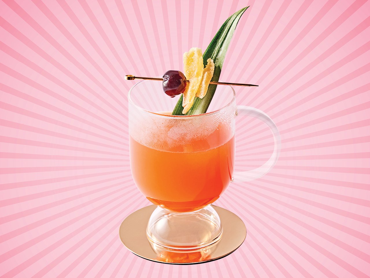 a glass mug with a pink hot drink inside garnished with a pineapple spear and a cherry