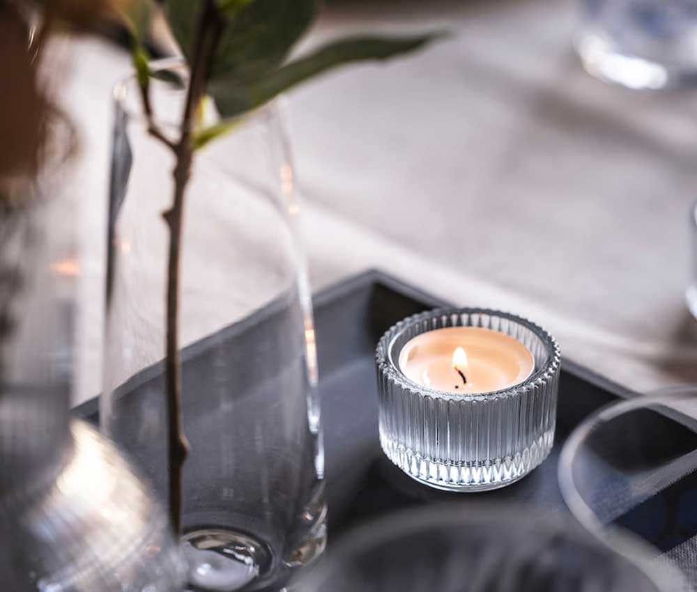 A ribbed glass tealight holder from Ikea pictured on a grey table filled with glass vases.